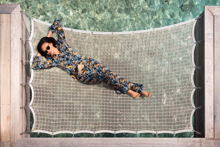 Femme allongée dans un hamac au-dessus du lagon pour Waldorf Astoria Maldives Ithaafushi aux Maldives.