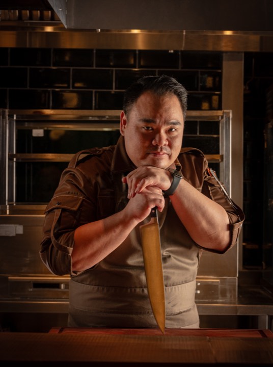 Portrait d’un chef tenant un grand couteau en cuisine pour Moutarde à Singapour.