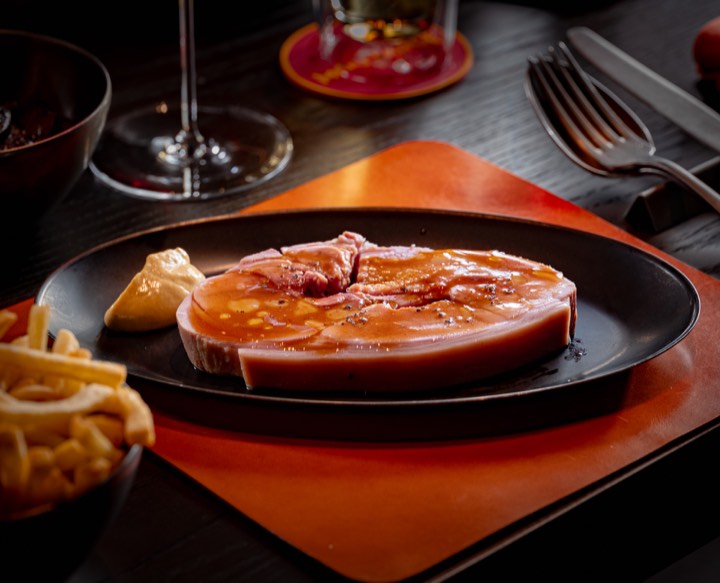 Une épaisse tranche de jambon dans une assiette noire pour Moutarde à Singapour.