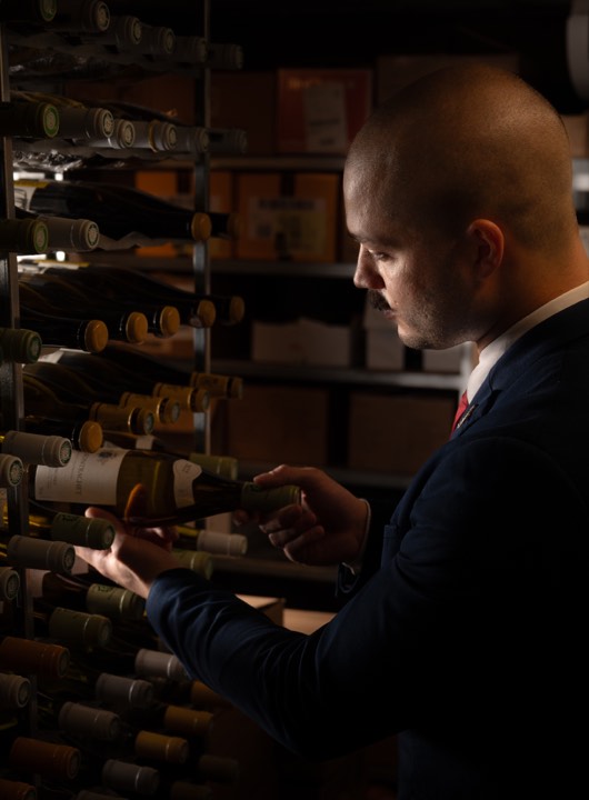 Le sommelier Clément Lopez qui prend une bouteille de grand vin pour L’Aparté à Toulouse.