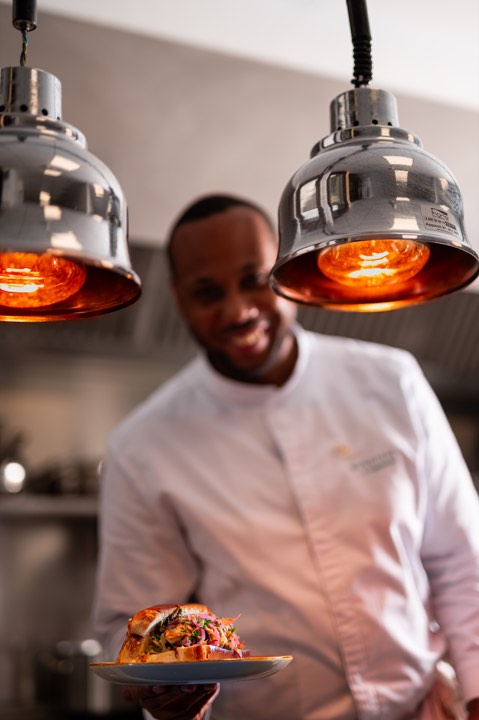Le chef Grégory Vingadassalon tendant une assiette au passe-plats pour Burdigala — Madame B à Bordeaux, France.