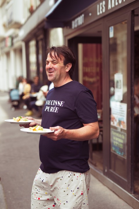 Le chef Thomas Brachet tenant deux assiettes devant son restaurant pour Les Arlots à Paris, France.
